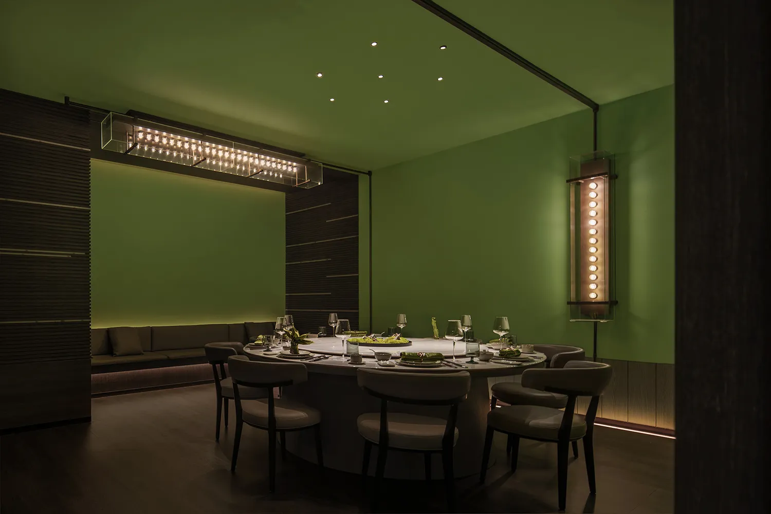 A modern restaurant dining room with dark green walls and illuminated lighting.
