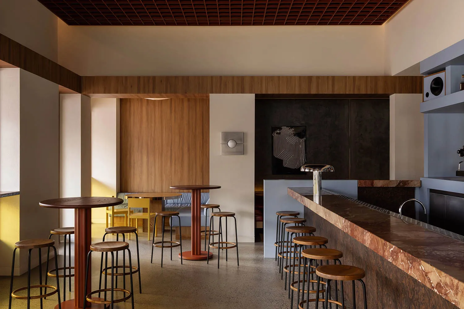 A modern restaurant bar with wooden tables and stools, featuring copper accents and a warm, inviting atmosphere.