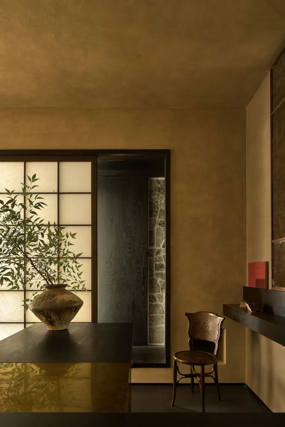 A minimalist interior design featuring a modern wall with a black door and a vase on a table.