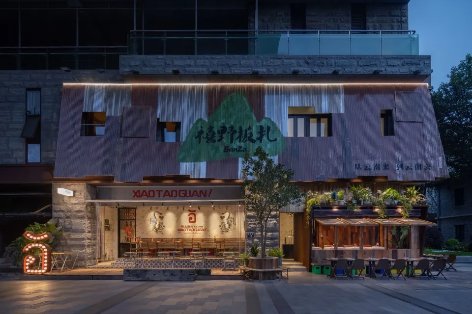 Modern restaurant exterior with metallic cladding, illuminated signage, and outdoor seating area.
