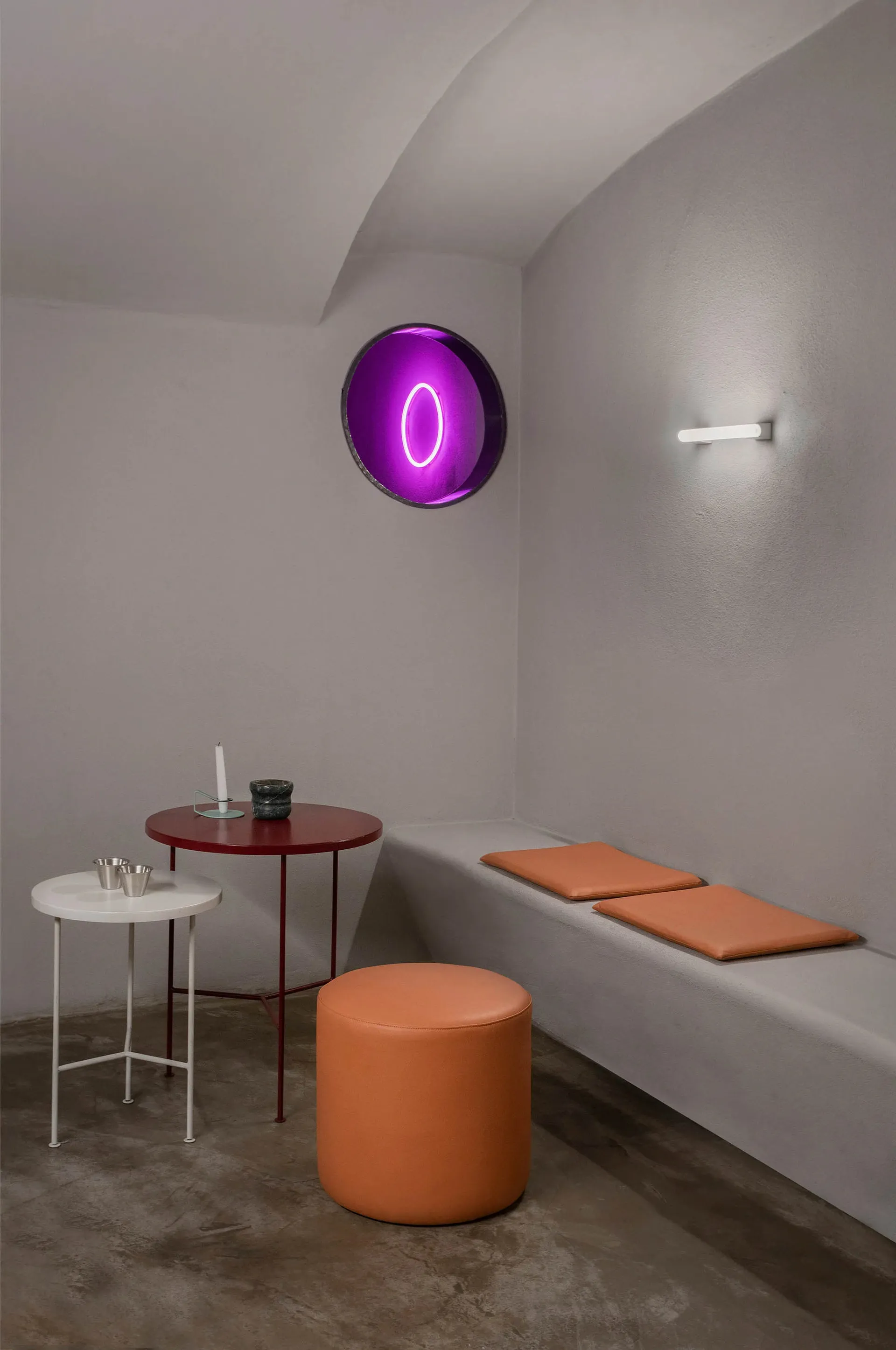 A minimalist living space with concrete walls, a white cushioned seat, and a purple illuminated object.