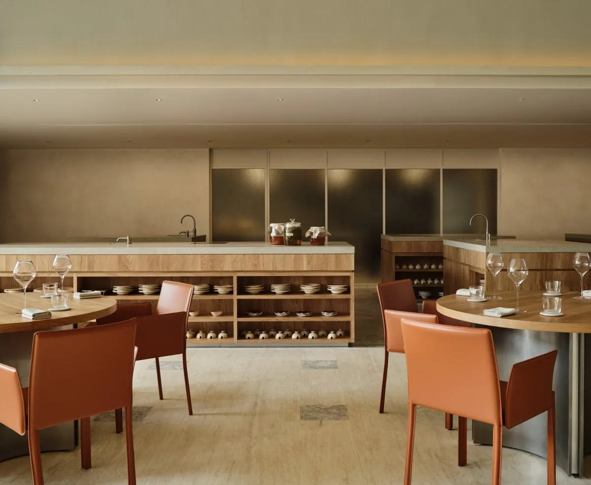 A modern restaurant interior featuring wooden furniture, concrete countertops, and glass elements.