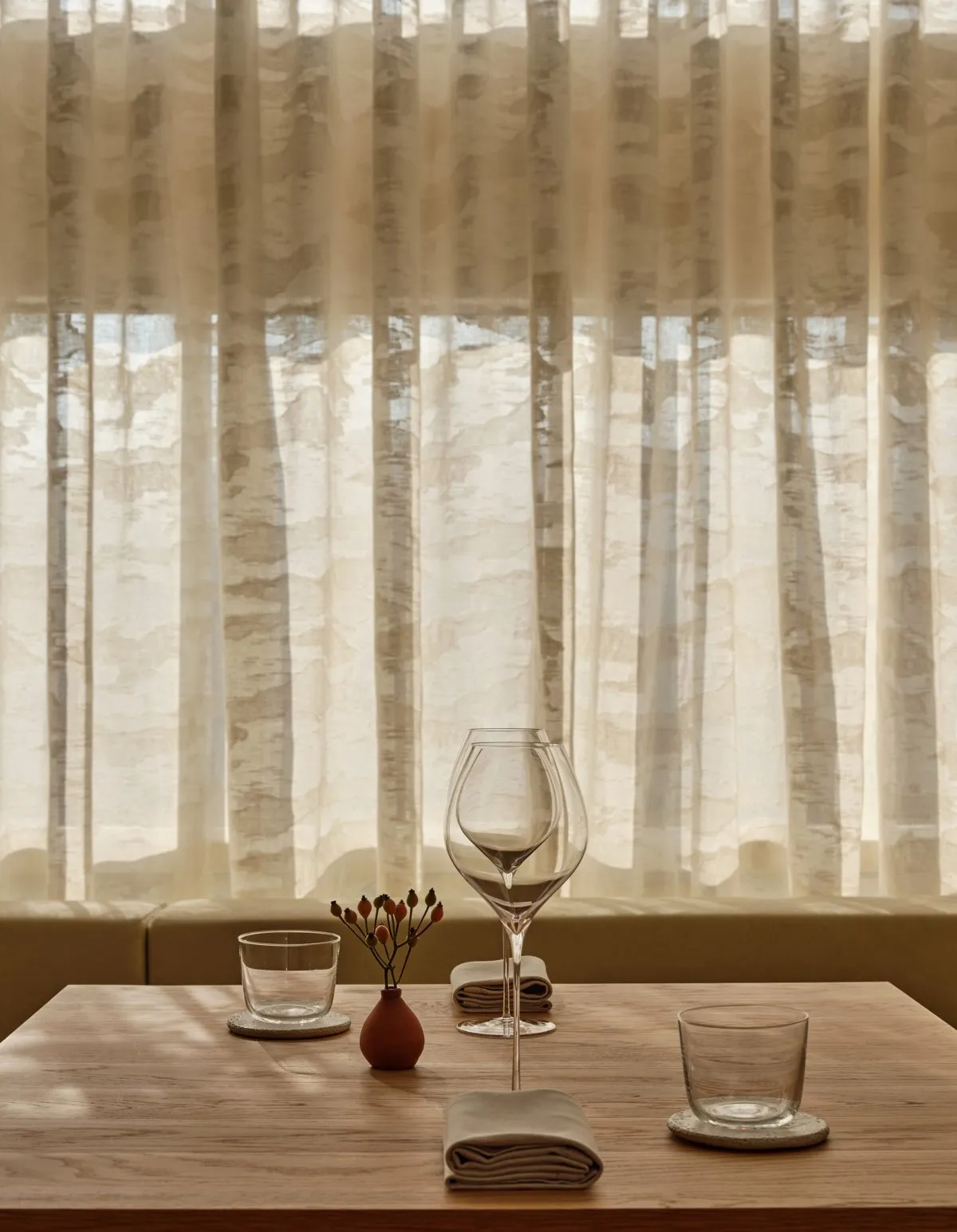 A minimalist restaurant table setting with natural fiber curtains in the background.