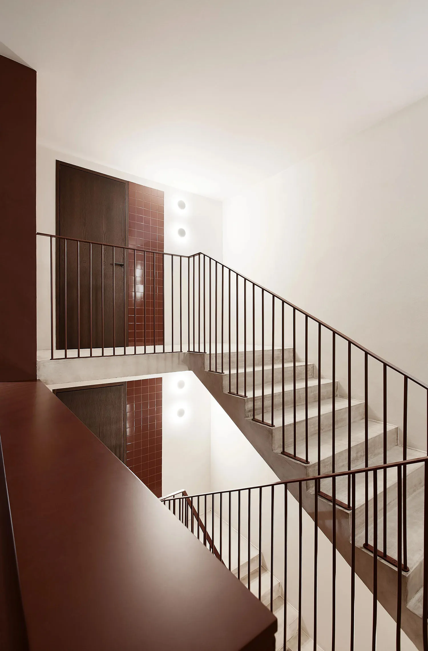 A modern interior space featuring a concrete staircase with dark railings and tiled walls.