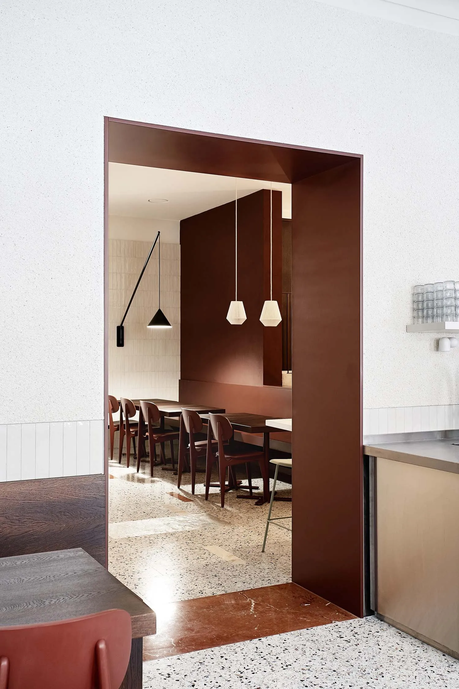 A modern minimalist restaurant interior featuring wood tables and terrazzo flooring.
