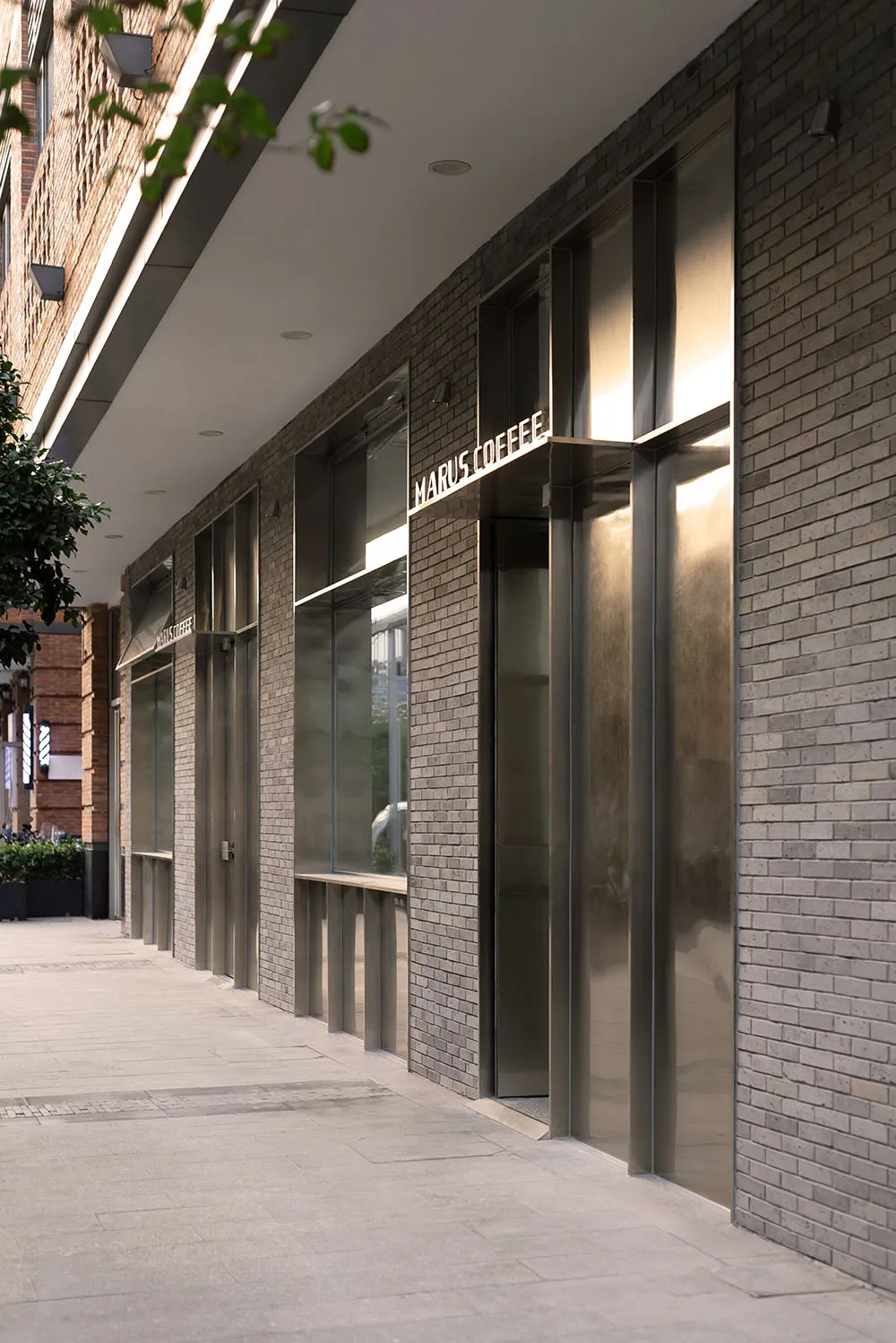 Retail storefronts with brick walls, glass windows, and metallic cladding on a city street.