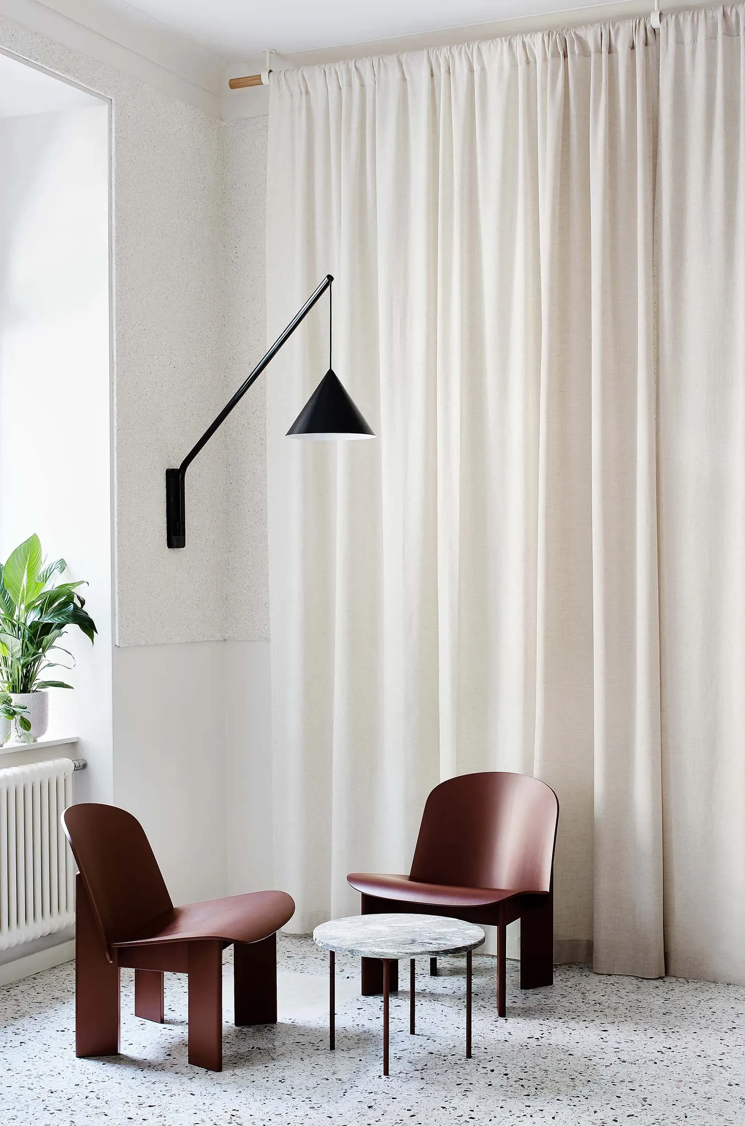 A modern lounge featuring fabric curtains, a metallic lamp shade, marble table, and resin floor.