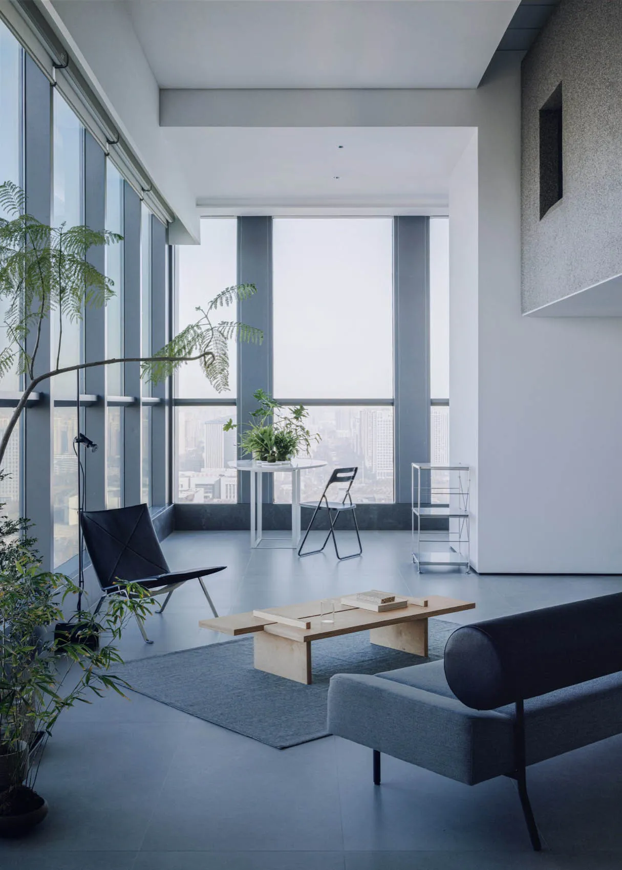 Modern minimalist living room with blue accents, featuring wooden coffee table, black leather chair, and large windows overlo