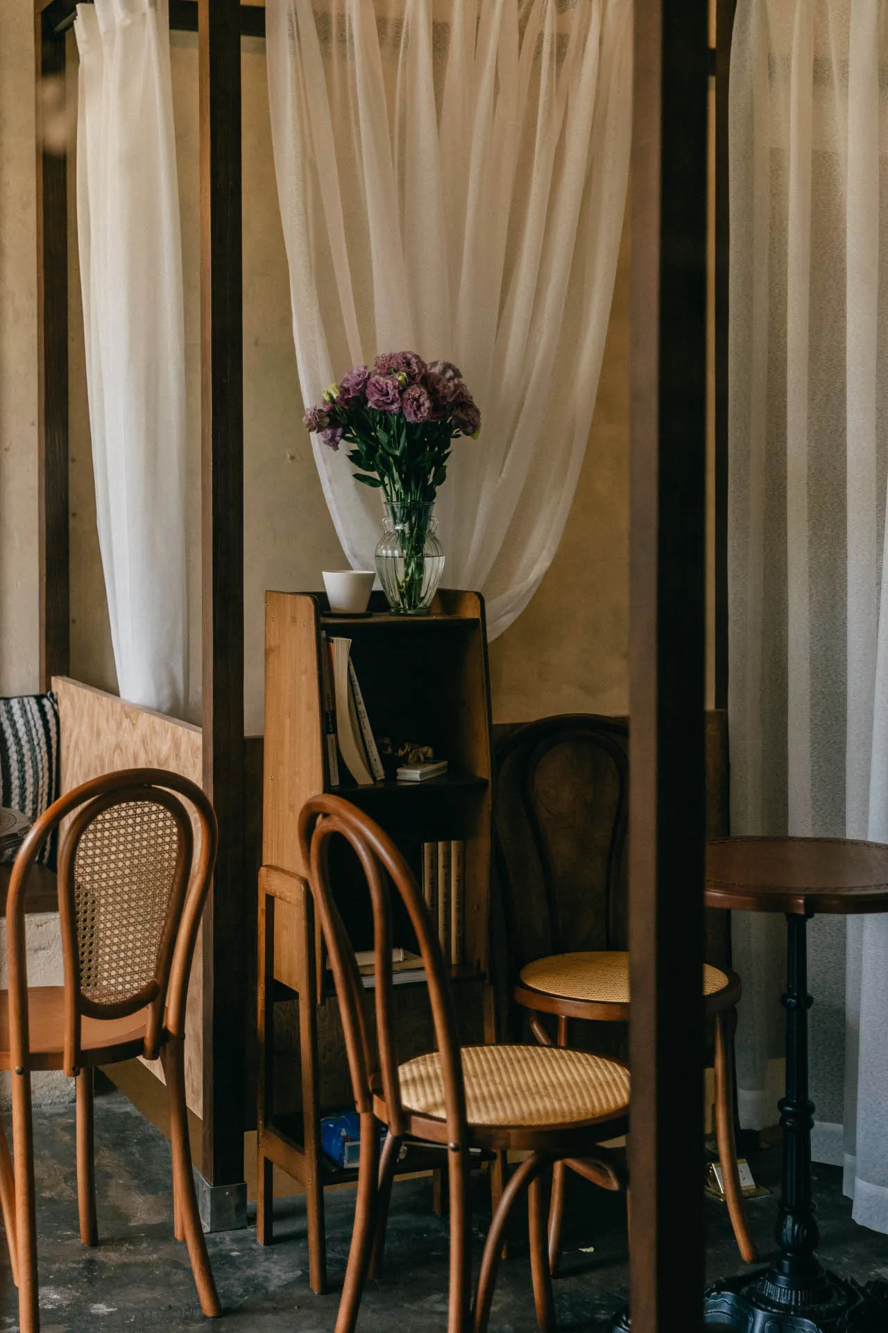 Industrial-style room with wooden shelves, chairs, and a vase of purple flowers.