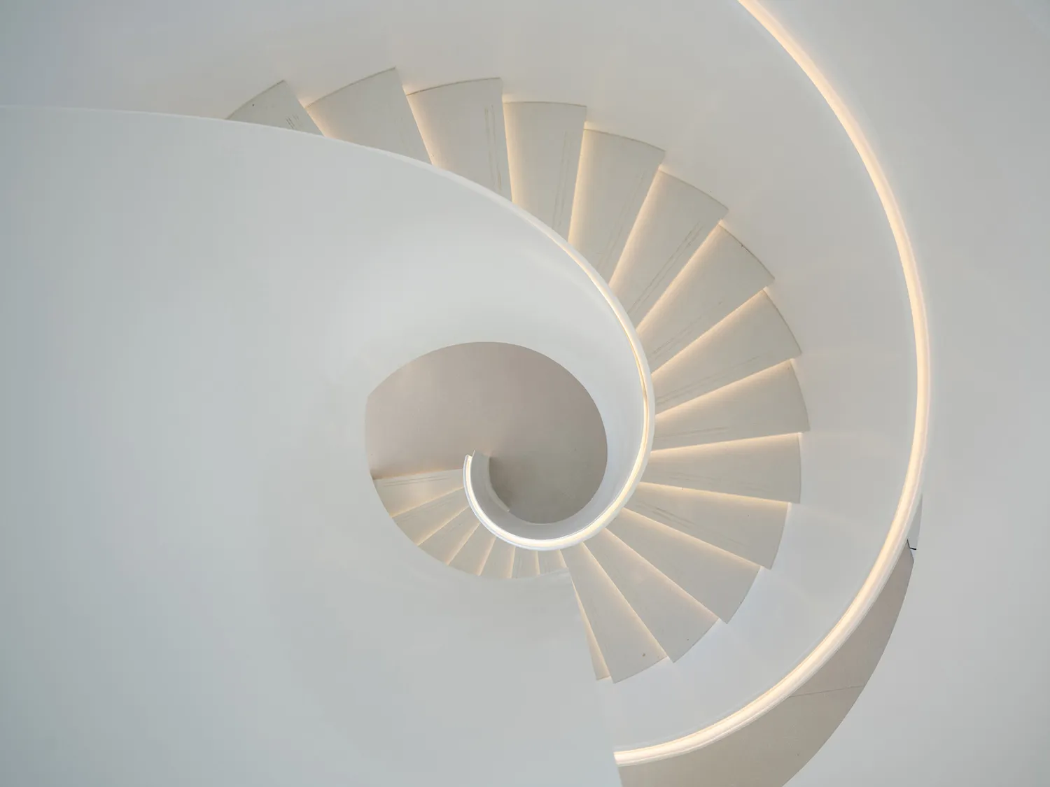 Modern, minimalist white concrete spiral staircase with illuminated edges.
