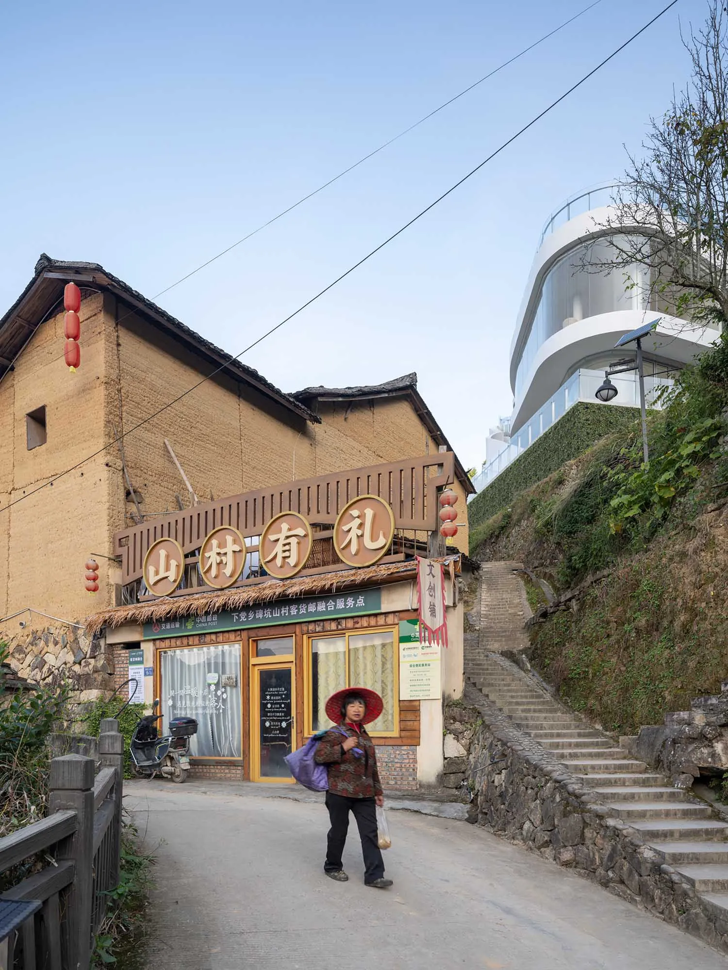 An old brick building sitting on a hillside street with a woman standing in front.