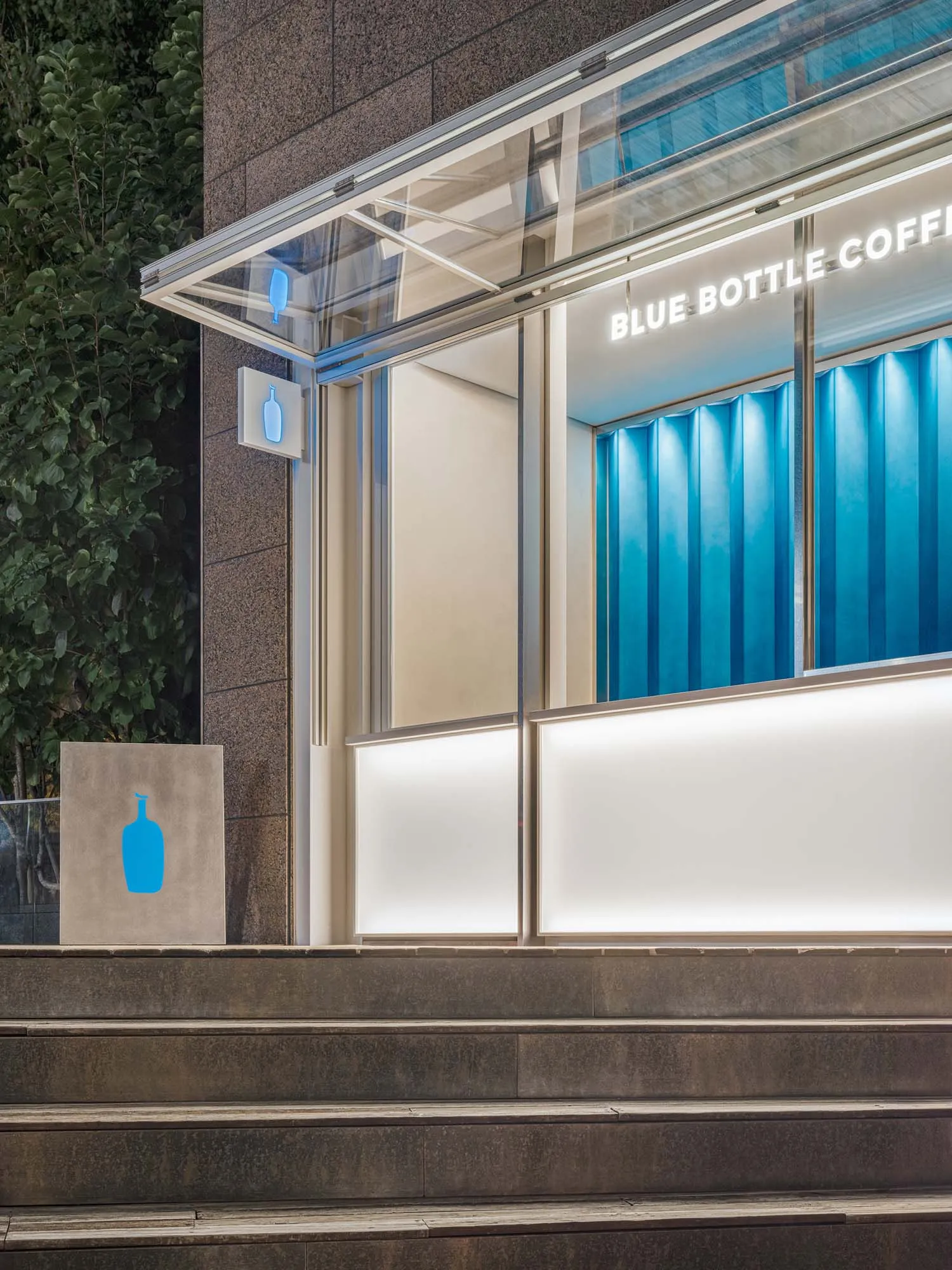 Modern storefront of Blue Bottle Coffee with glass walls and blue lighting