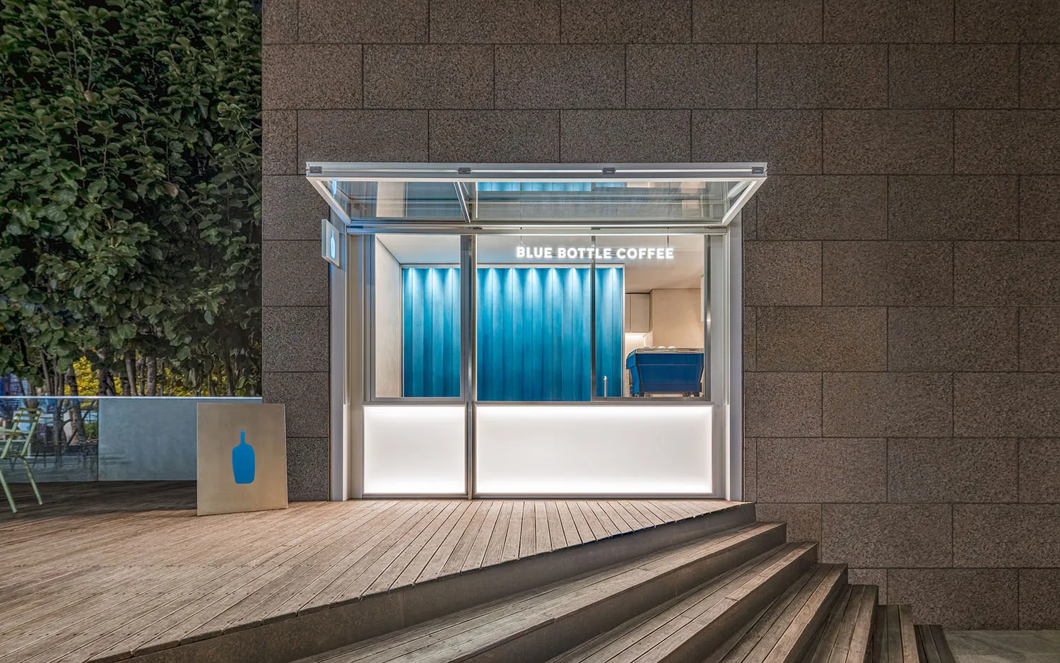 Modern minimalist exterior of a Blue Bottle Coffee location featuring glass elements.