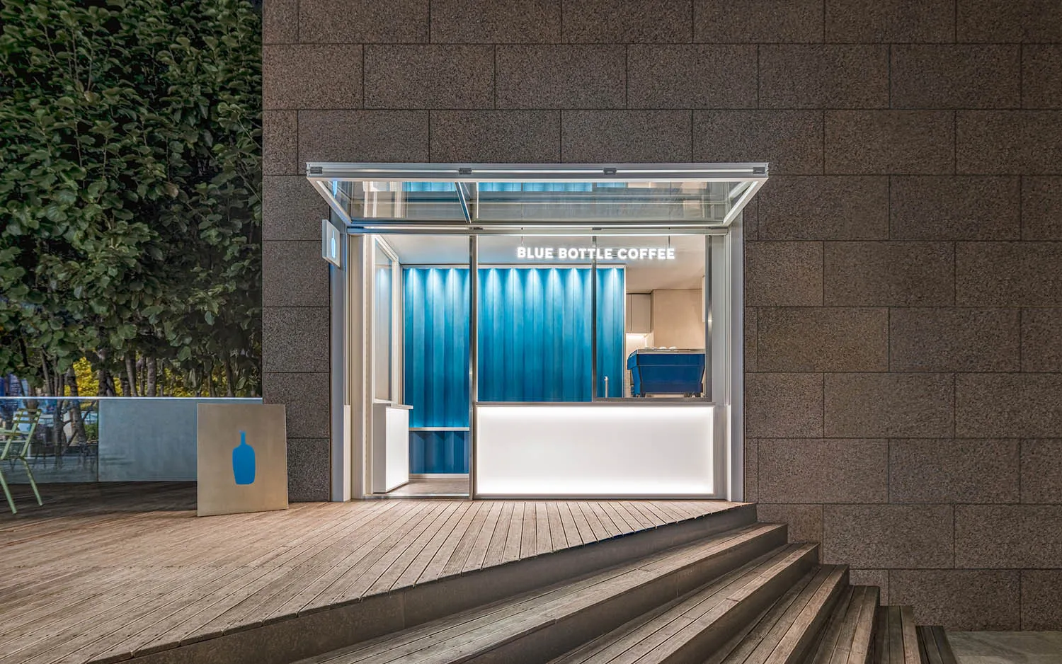 Modern, sleek glass entrance to a coffee shop with blue accents and white counter.