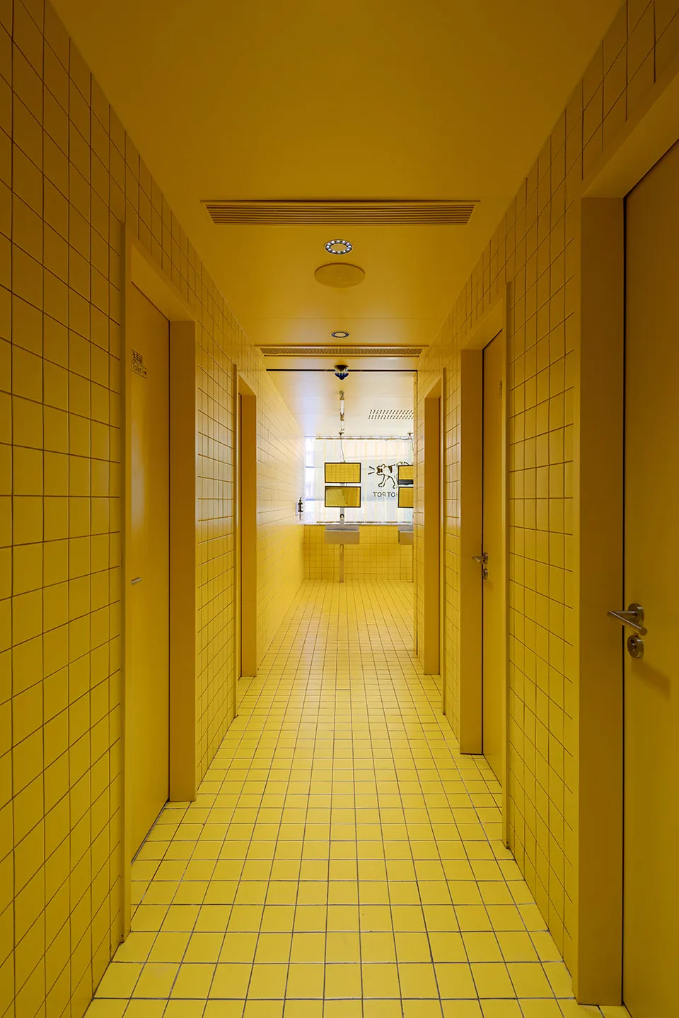 A minimalist public restroom with yellow tiled walls and floor.