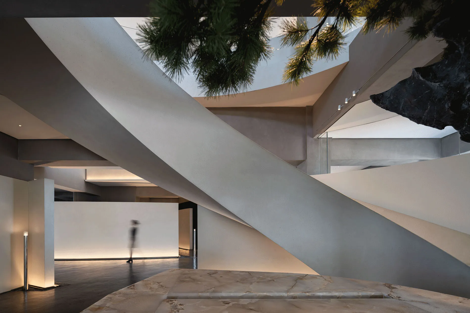 Modern commercial interior with concrete walls and floors, featuring a central staircase and skylight.