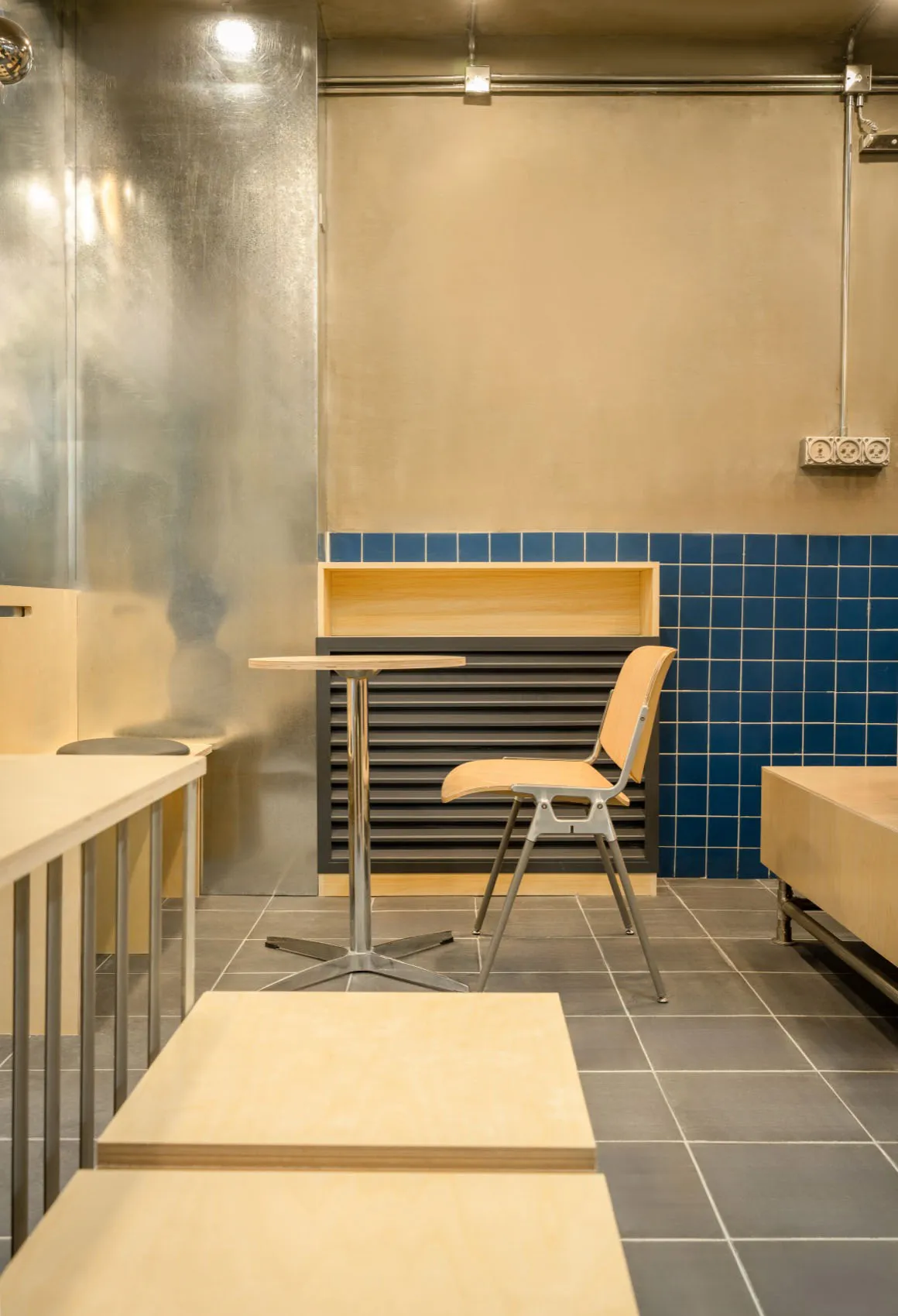 A minimalist cafe dining room with wooden tables, metal chairs, and blue tiled walls.
