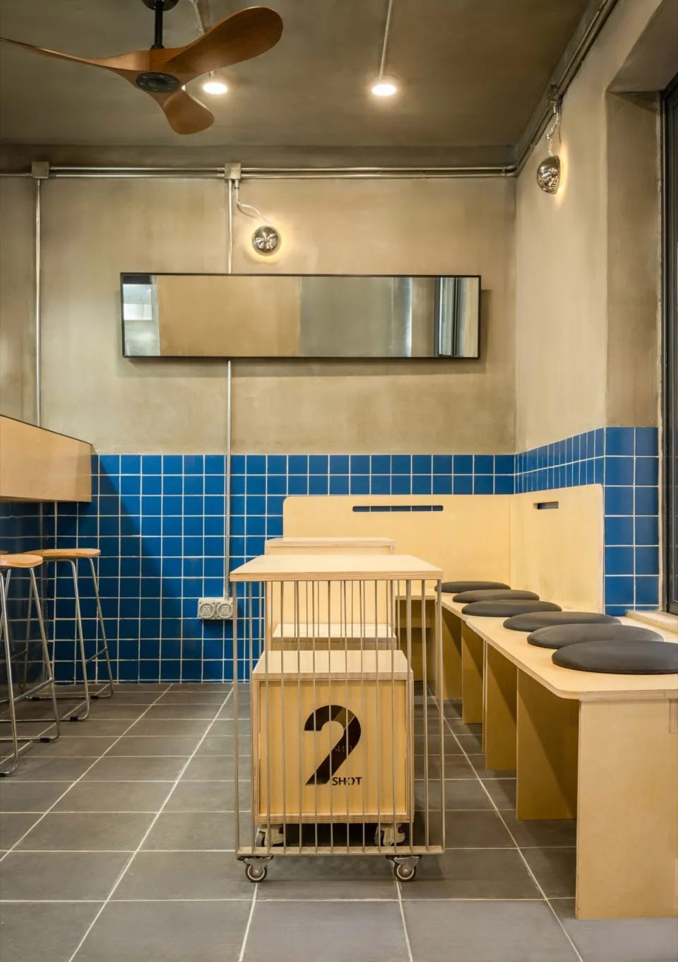 現代工業風餐廳室內,藍色瓷磚牆搭配木製餐桌與金屬吧凳。