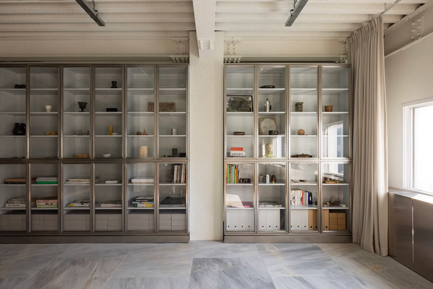A large industrial-style glass bookcase filled with books, vases, and decorative objects.