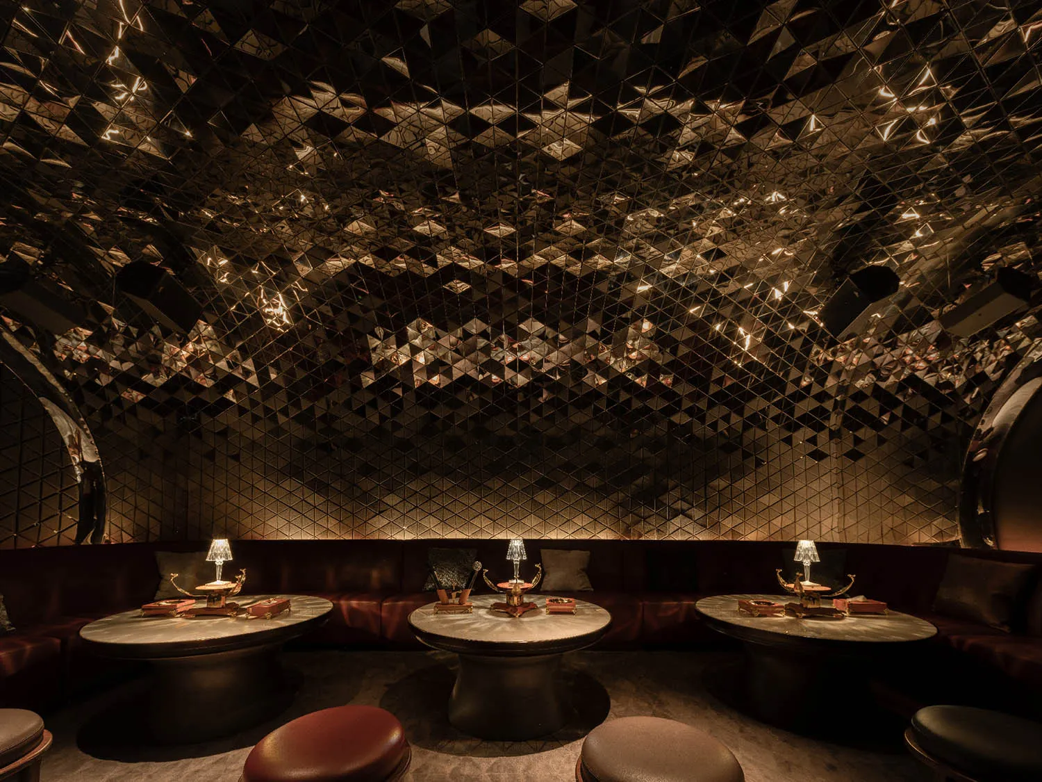 A luxurious nightclub interior with metallic tiles on the ceiling and walls, featuring round tables and plush seating.