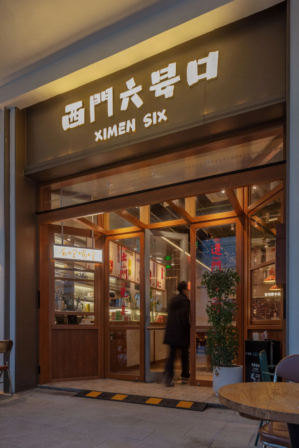 A modern restaurant exterior with glass doors, wooden accents, and a sign with Chinese characters and English text.