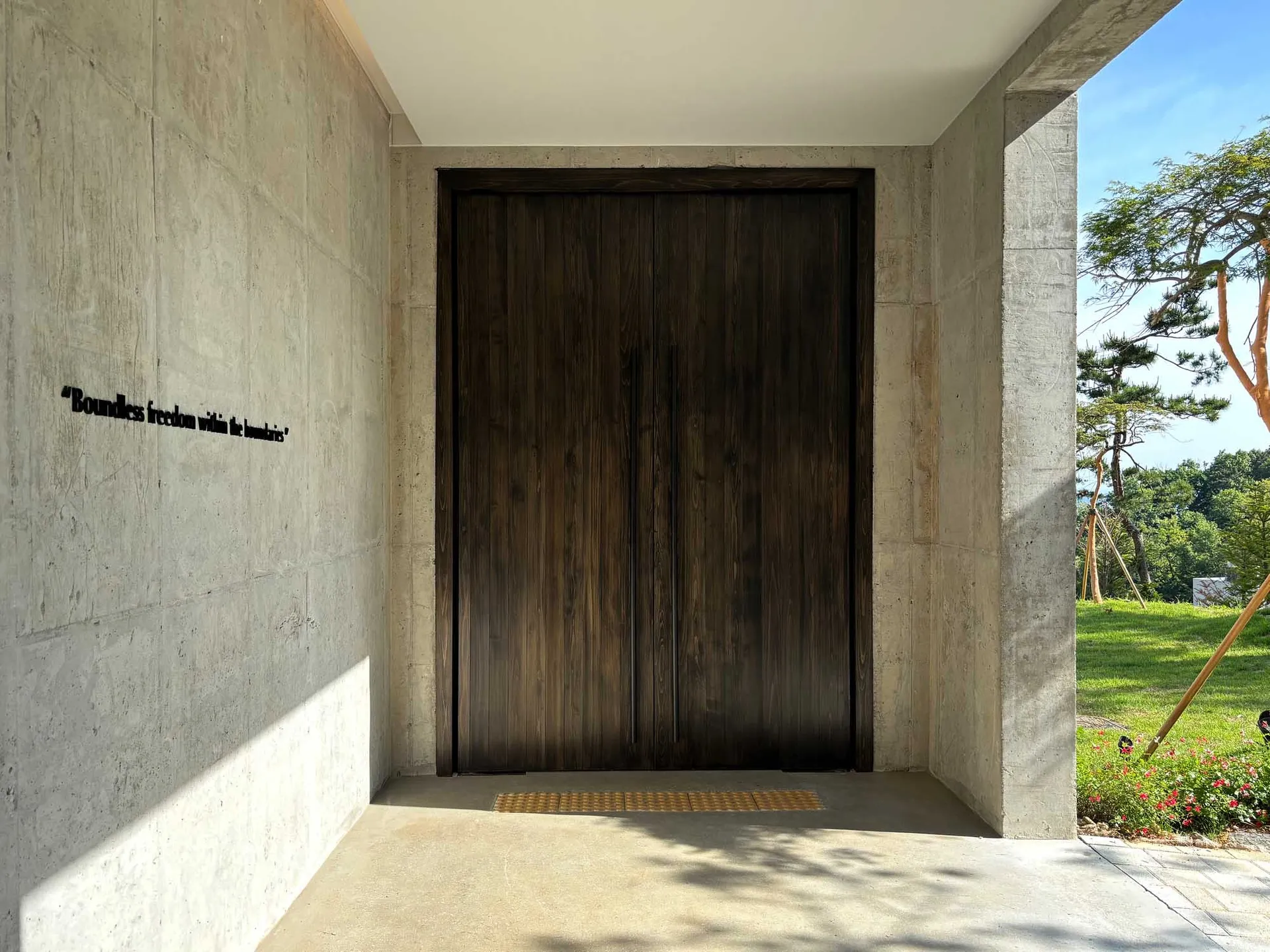 A modern entryway featuring a dark wood double-door with a concrete base and a quote 'Boundless freedom within the boundaries