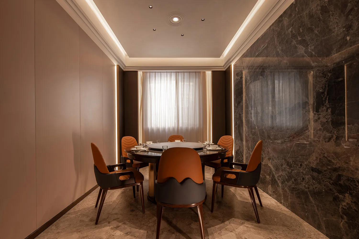 Modern dining room with marble flooring and walls, featuring a round table and orange chairs.
