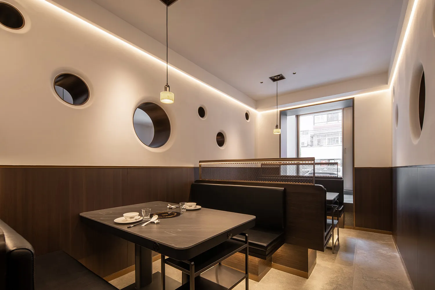 A modern restaurant interior with booth seating, glass pendant lights, and round windows
