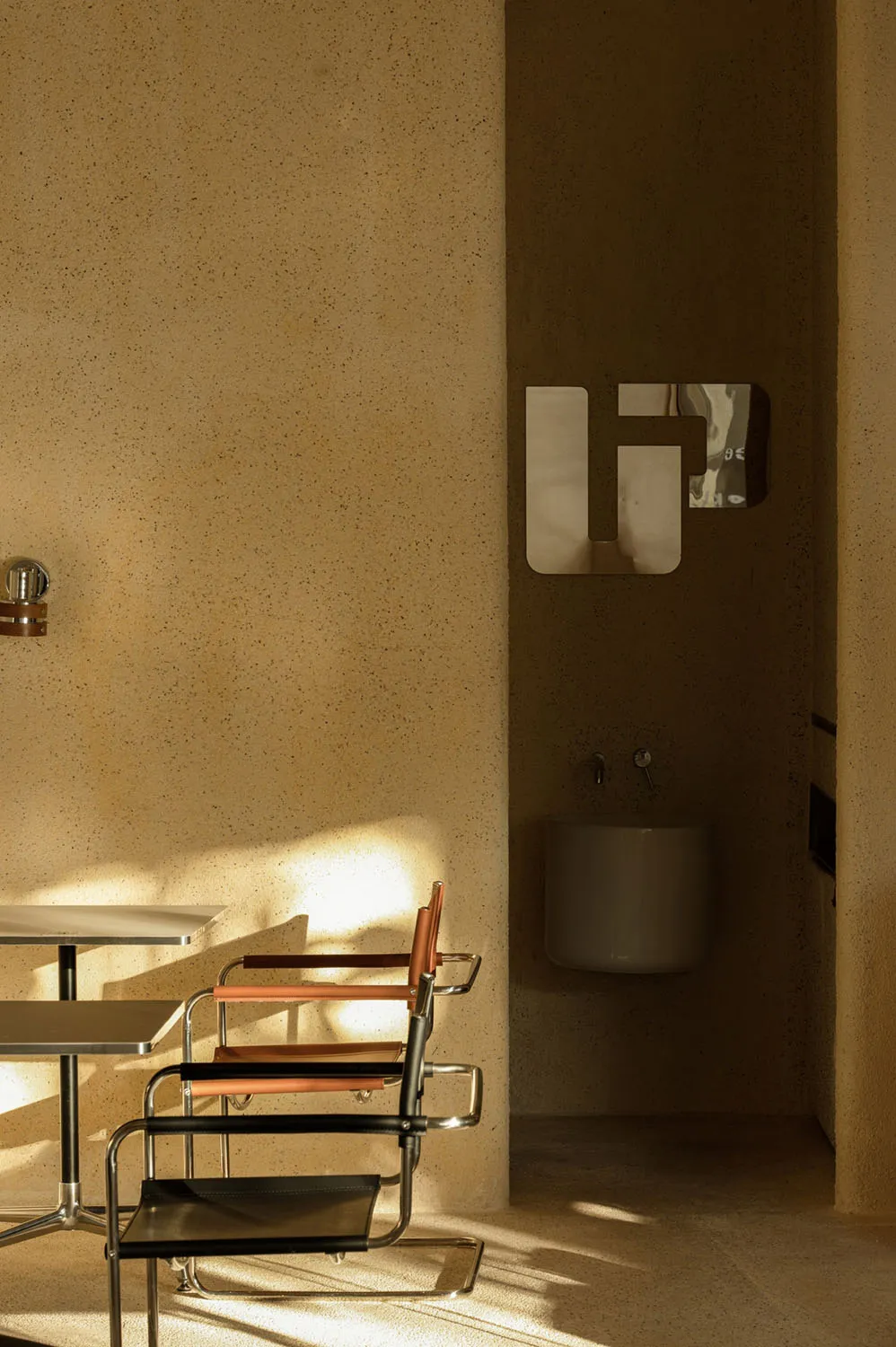 A minimalist interior with a concrete wall and floor, featuring modern furniture and a small mirror.
