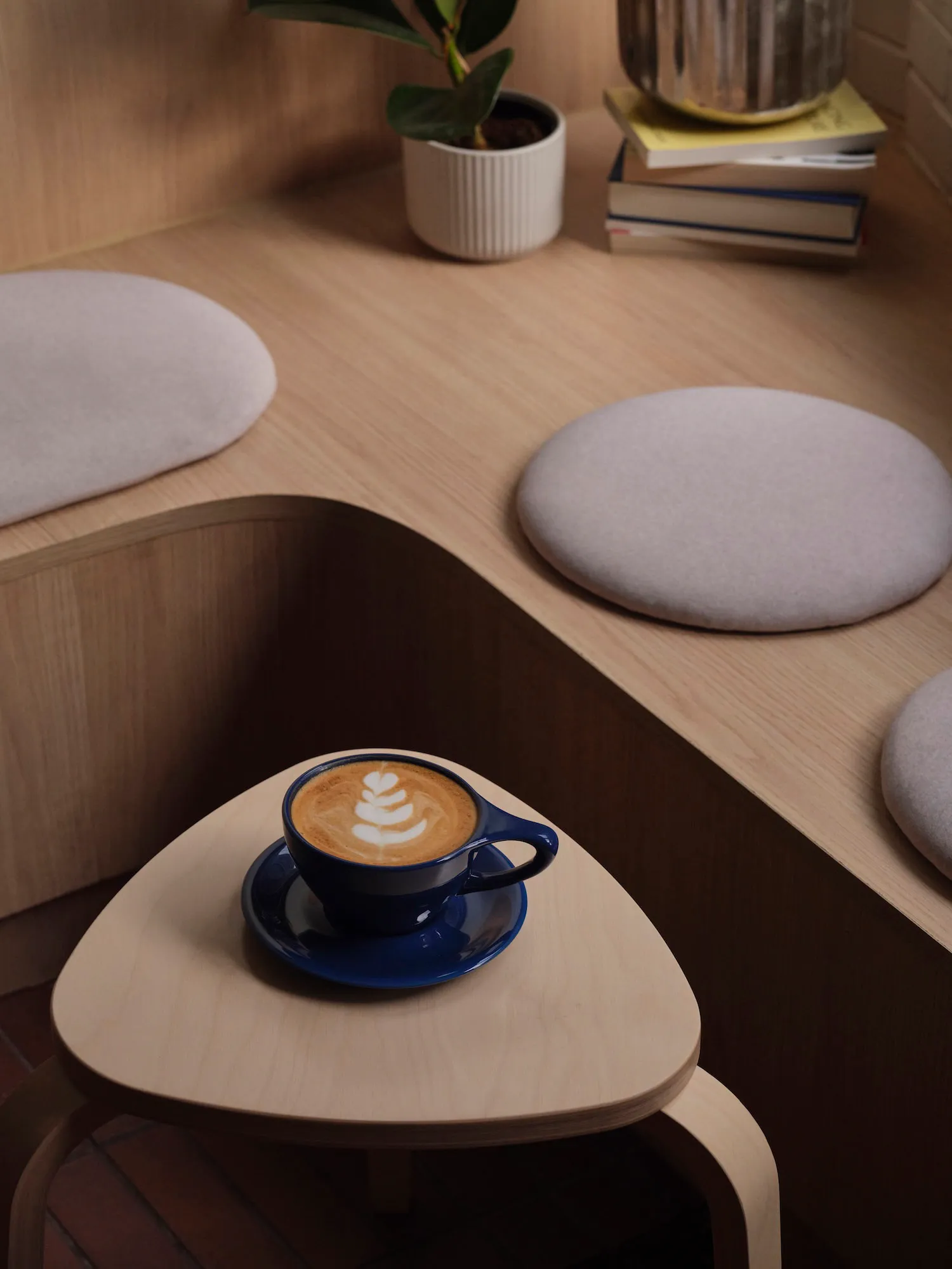 A cozy coffee shop interior with a wooden table featuring a blue ceramic coffee cup with latte art, surrounded by upholstered