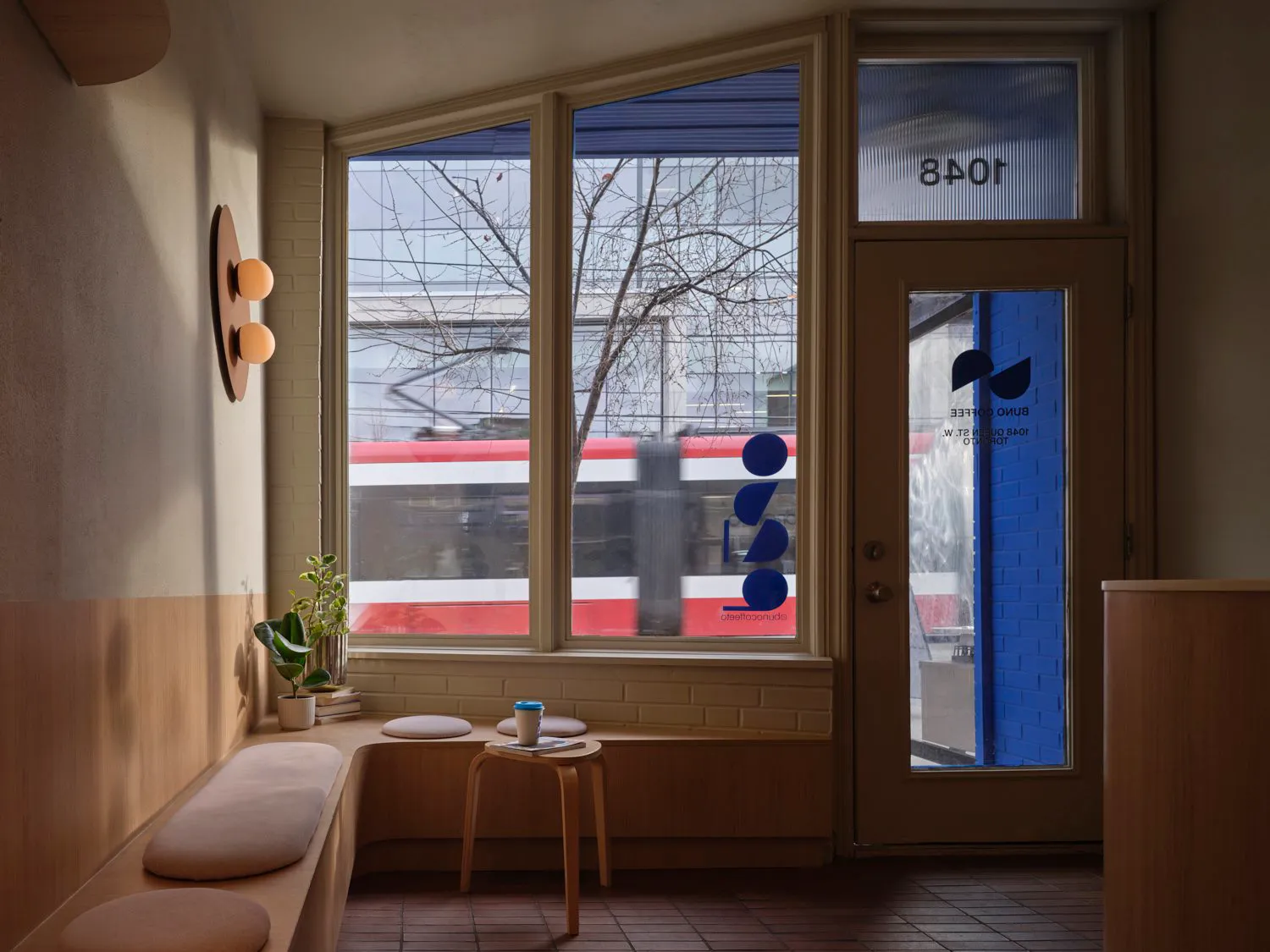 A cozy coffee shop interior with large windows, wooden seating, and brick and glass elements.