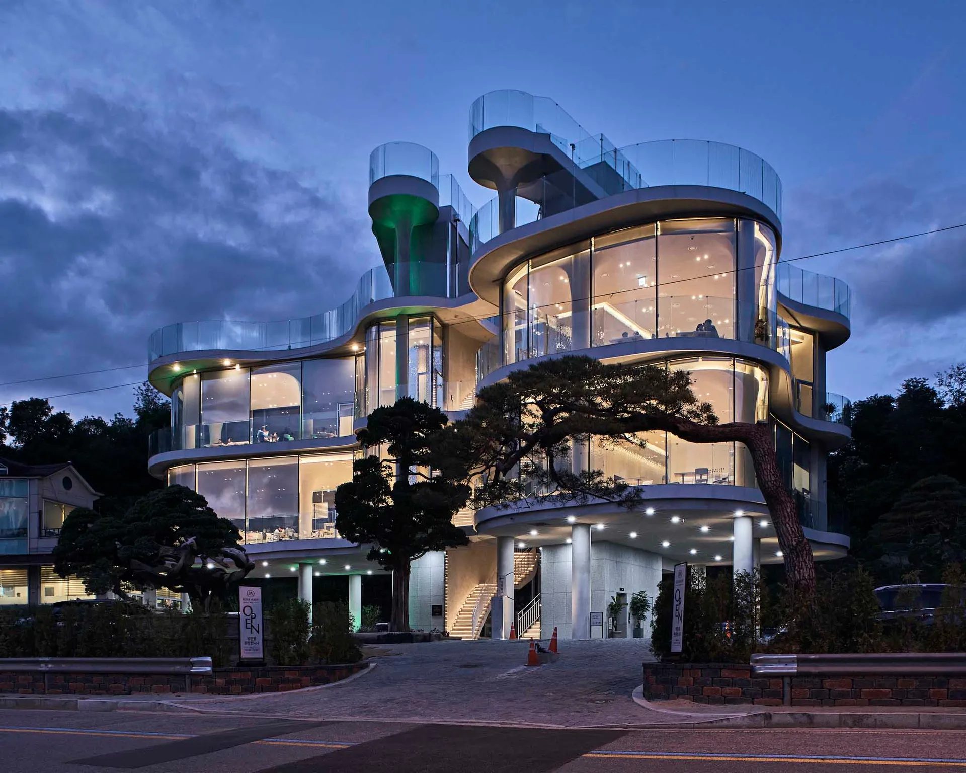 A modern glass restaurant with curved design and illuminated interior.
