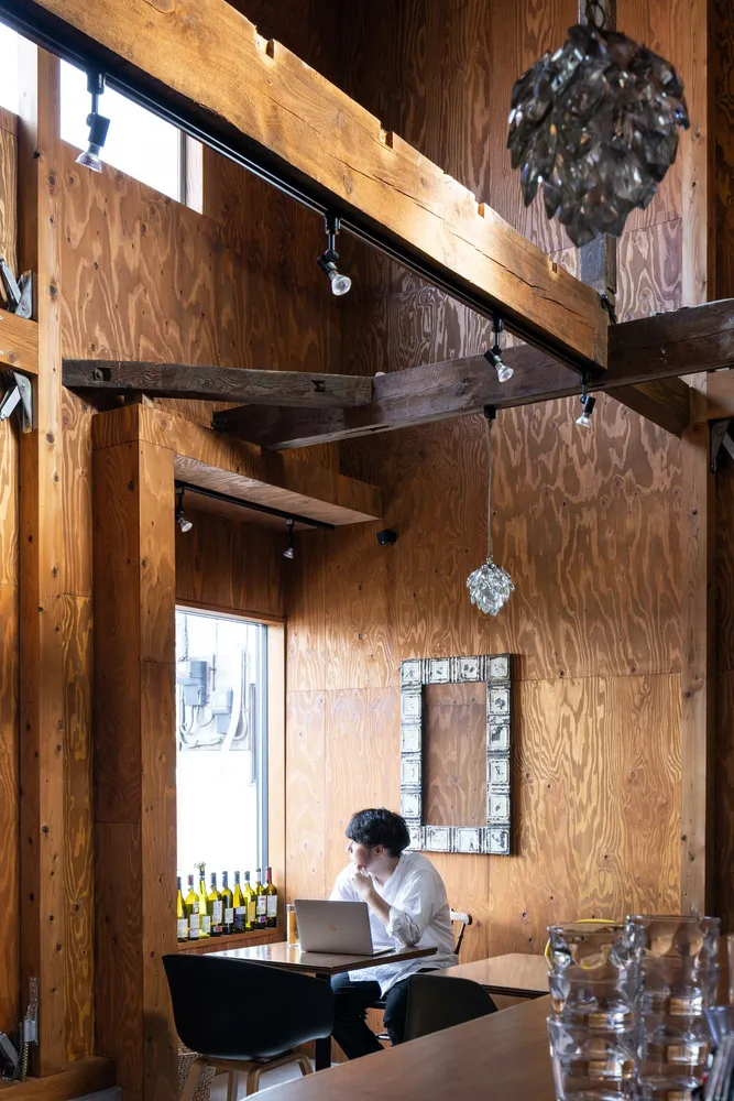 Person using laptop in a modern cafe with wood-paneled walls and a large window showcasing bottles of wine on a ledge.
