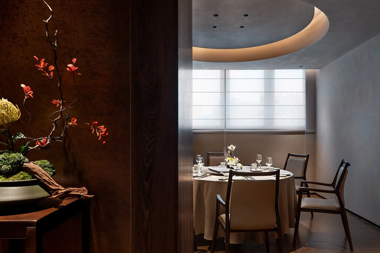 A modern restaurant interior featuring a table set with white tablecloth, chairs, and floral centerpiece.