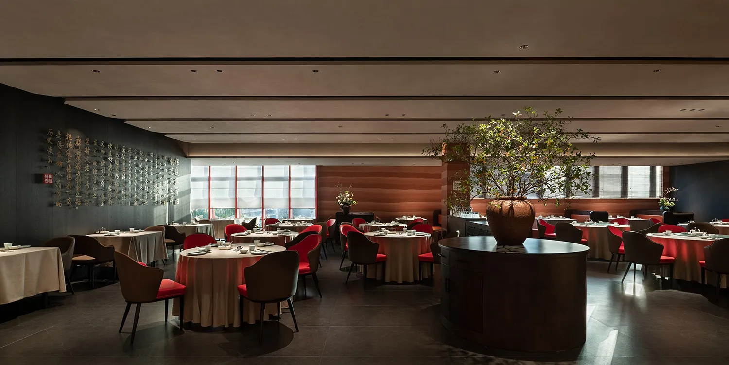 A modern restaurant interior with marble walls, glass tables, and fabric chairs.