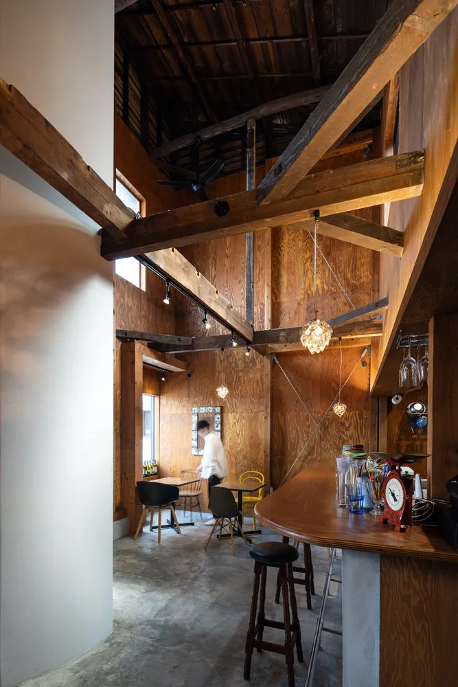 Industrial-style restaurant interior with wooden beams, tables, stools, and a bar area.