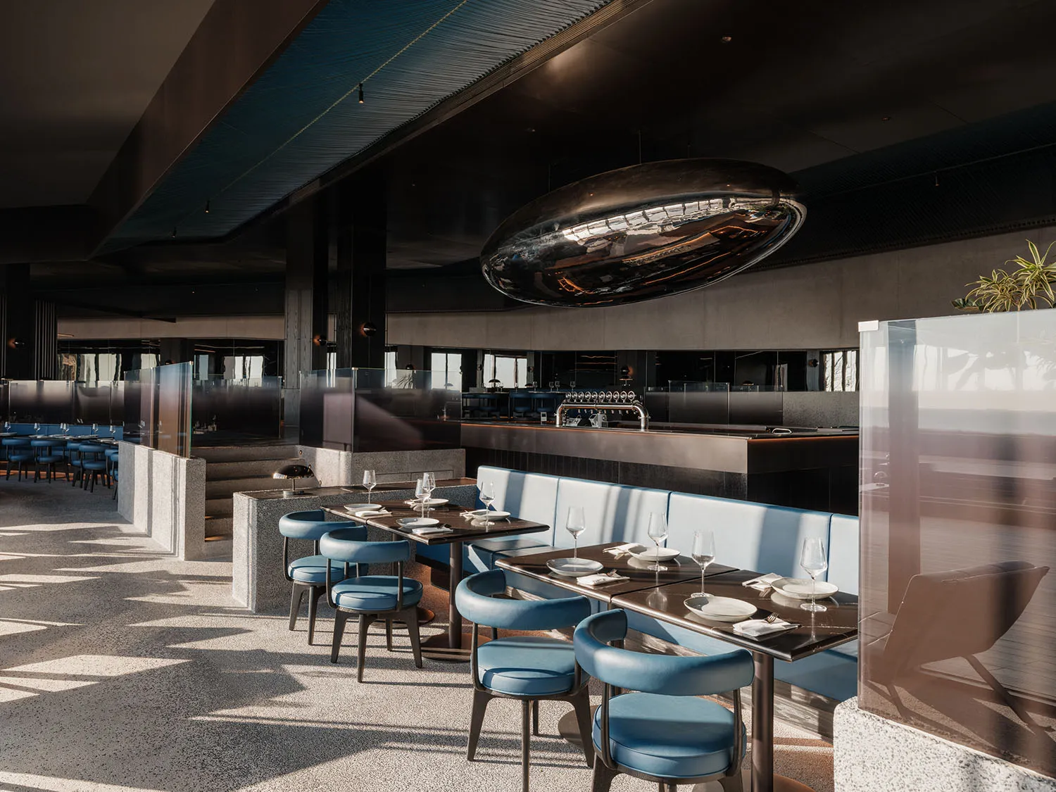 A modern, minimalist restaurant interior featuring metal, concrete, and leather materials.