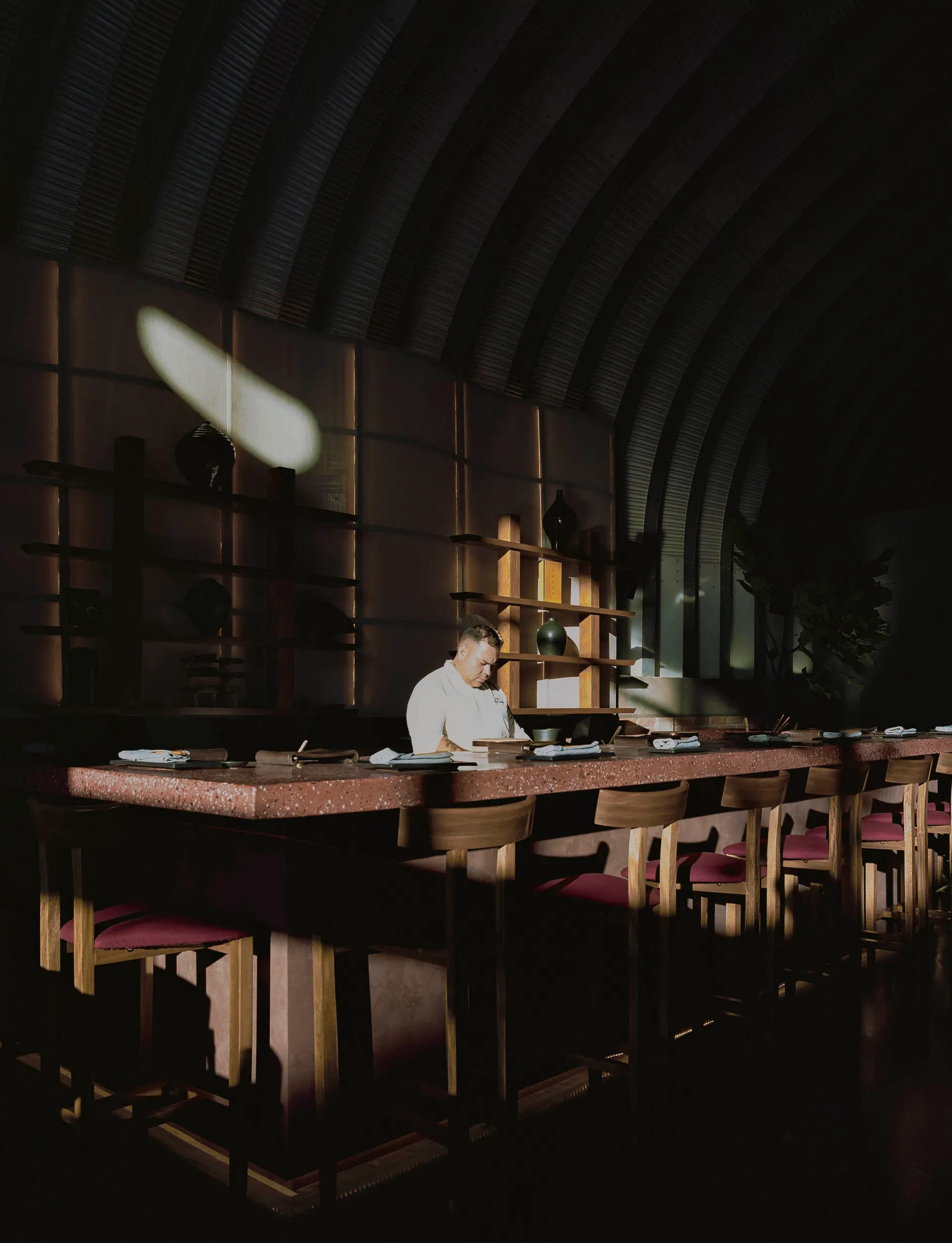 A chef preparing food behind a terrazzo counter in a restaurant interior with a dark, minimalist design.