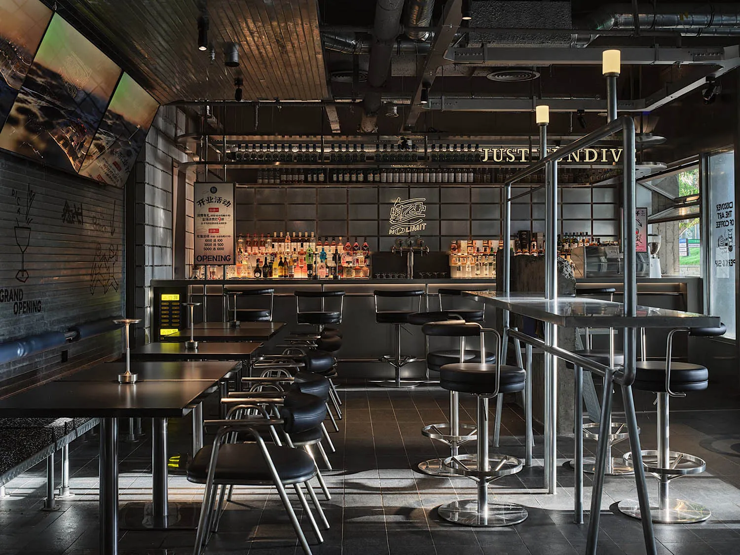Industrial-style restaurant bar with metallic tables, stools, and a well-stocked bar area.