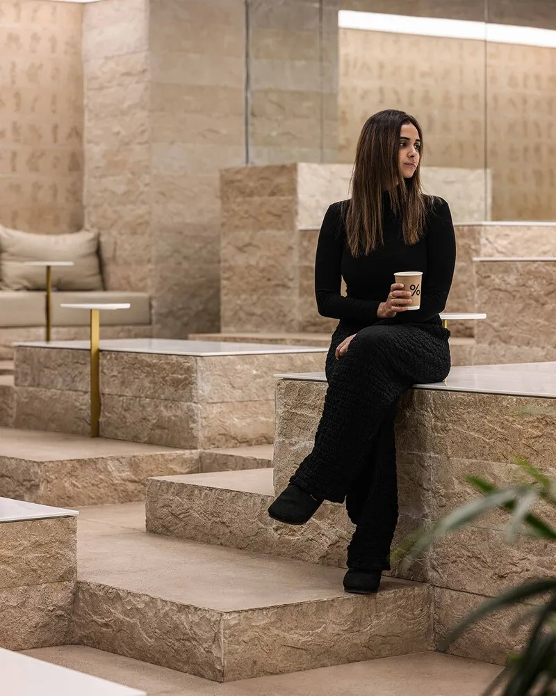 A woman sitting in a modern stone cafe space with a coffee cup in her hand.