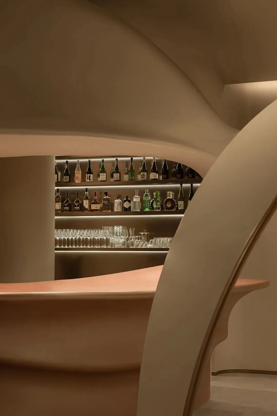 A modern bar with glass shelves displaying bottles of spirits and glasses.