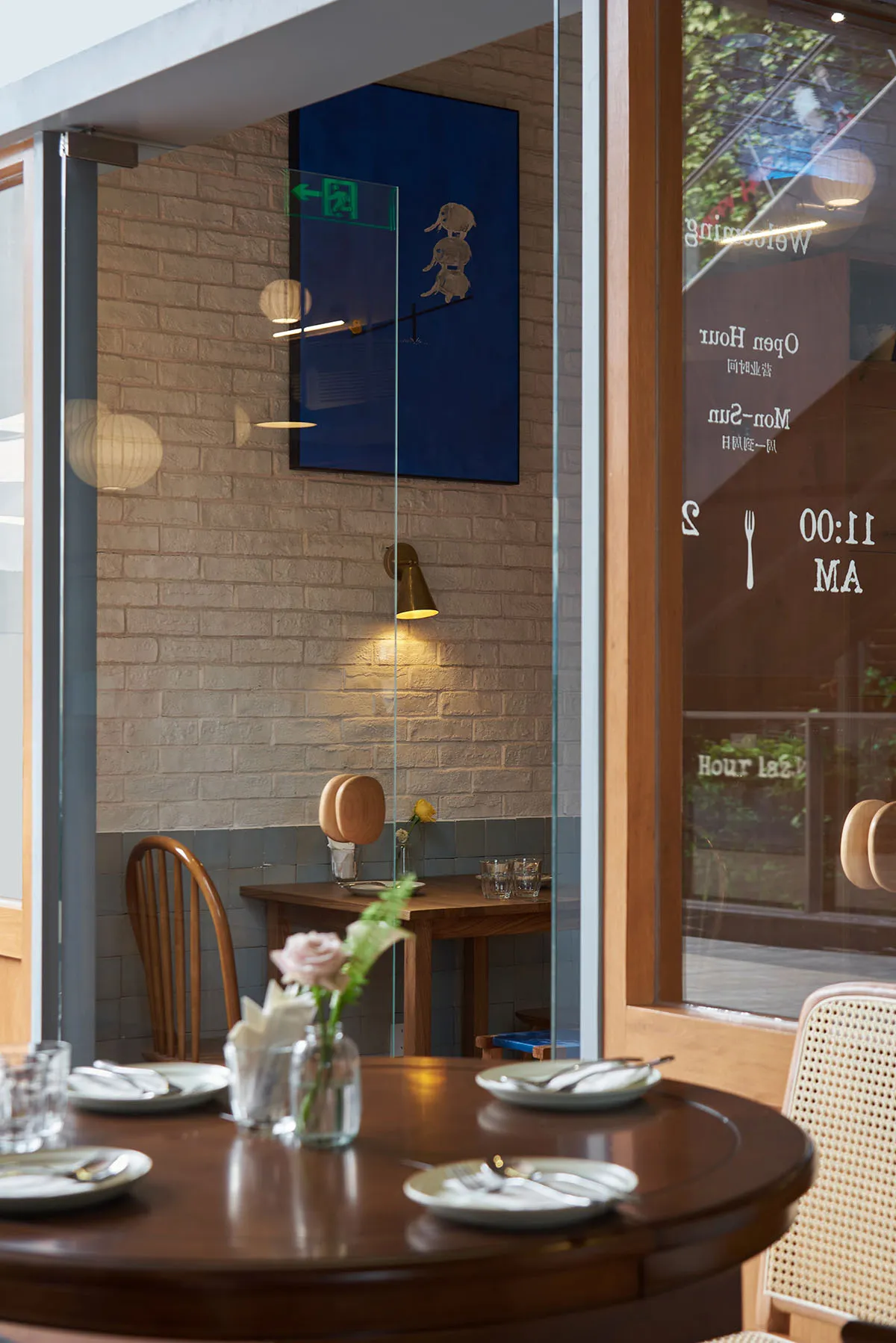 A cozy restaurant interior with wooden tables and chairs, a warm light fixture, and a brick wall.