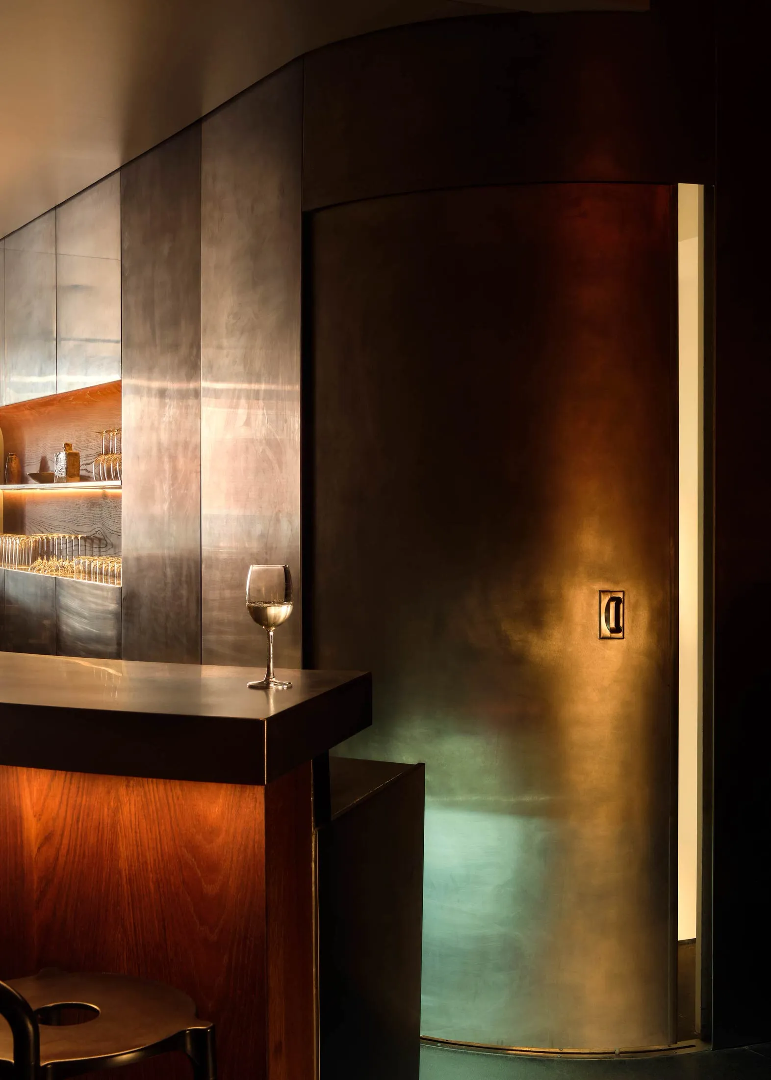 A modern industrial bar with a metal-clad wall and a glass of wine on the counter.