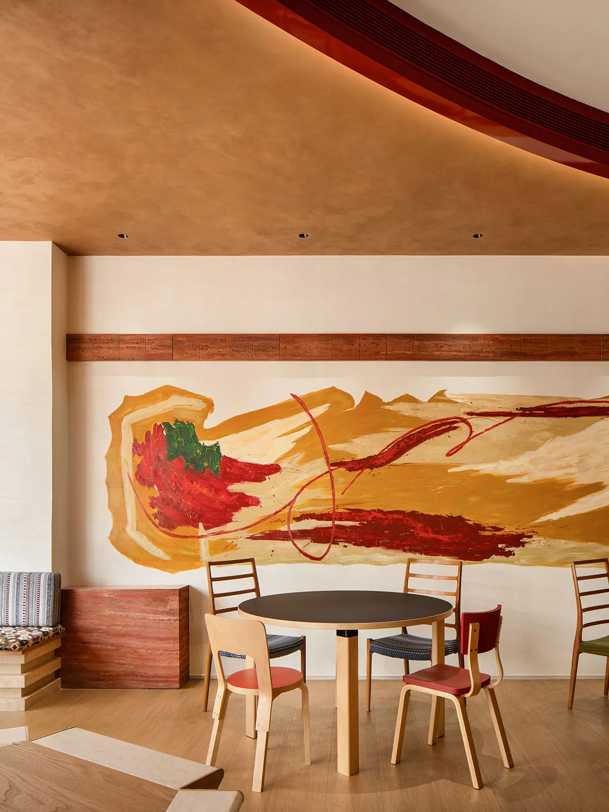 A modern rustic restaurant interior with a large abstract mural, wooden tables, and colorful chairs.