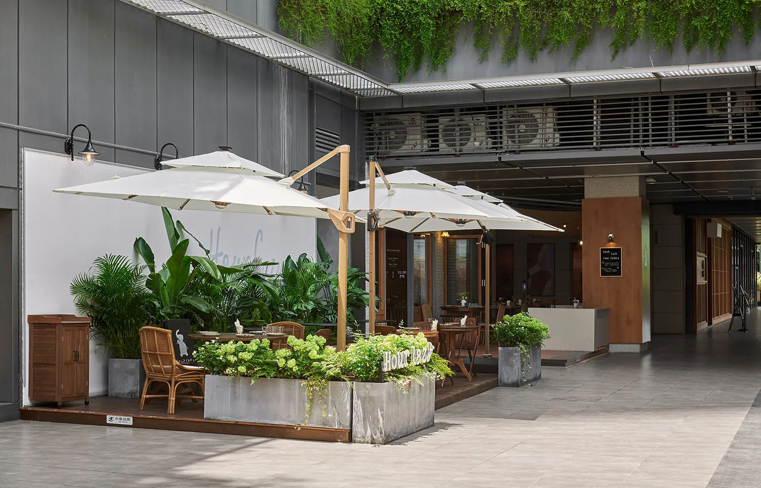 An industrial outdoor seating area with concrete tables, wooden chairs, and large umbrellas.