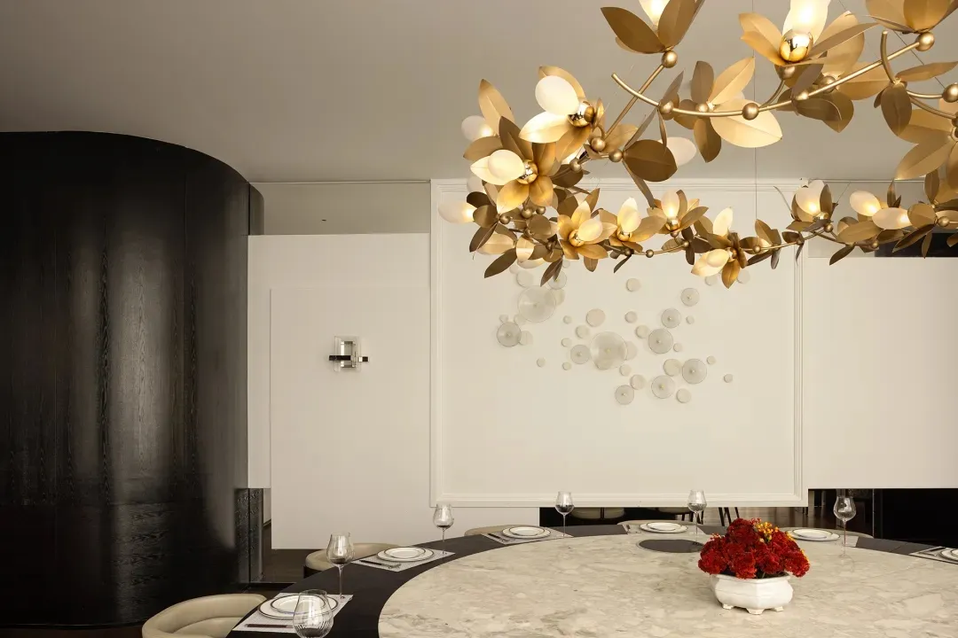 Modern dining room featuring a round marble table, elegant tableware, and a gold floral light fixture
