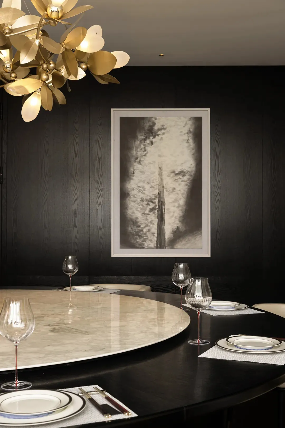 A modern dining room featuring a round marble table with elegant place settings and a sophisticated chandelier.