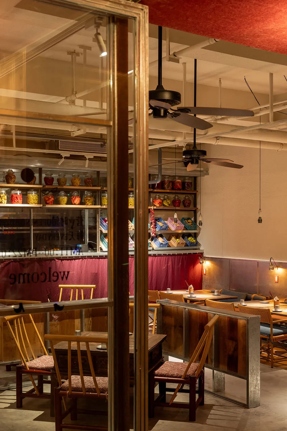 Industrial-themed restaurant interior with wooden furniture and shelves displaying jars and baskets.