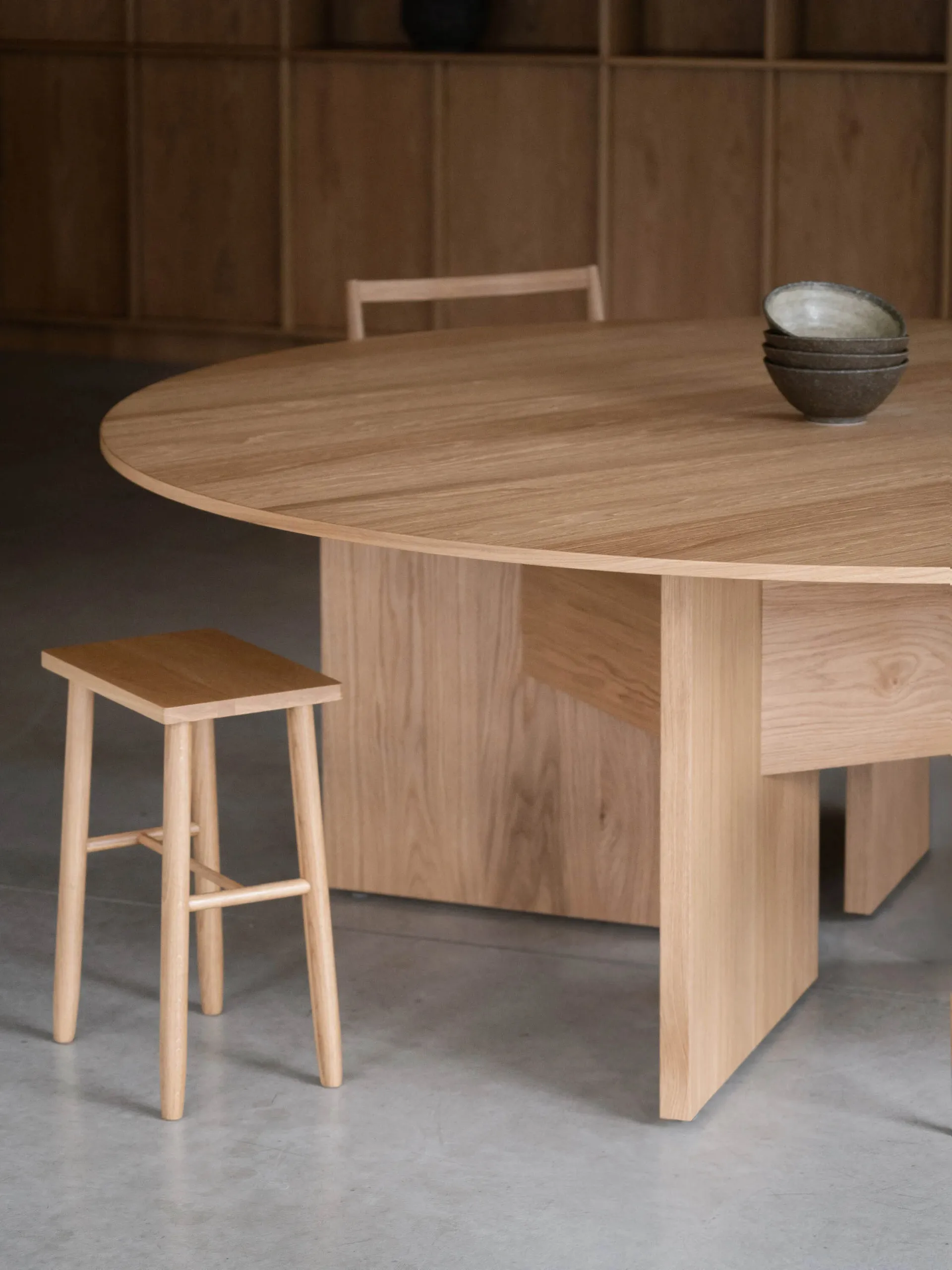 A minimalist dining room with a wooden table and stool, focusing on natural wood textures and a serene aesthetic.