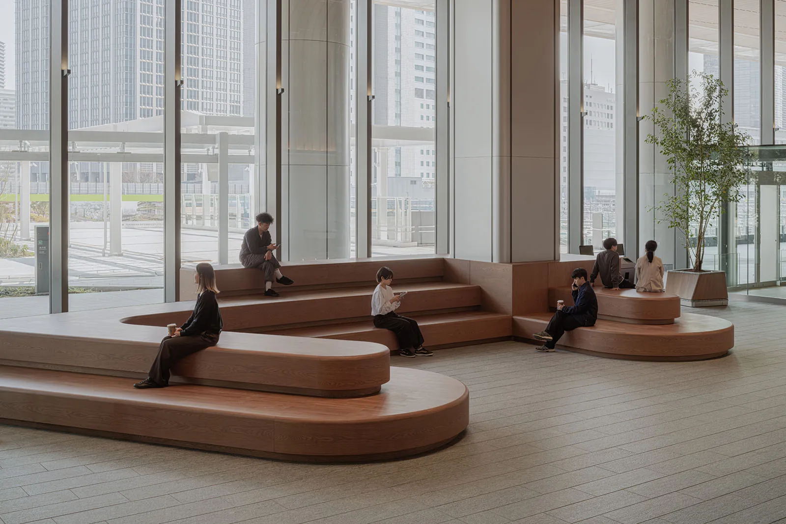 People working in a minimalist office space with wooden seating and large windows.